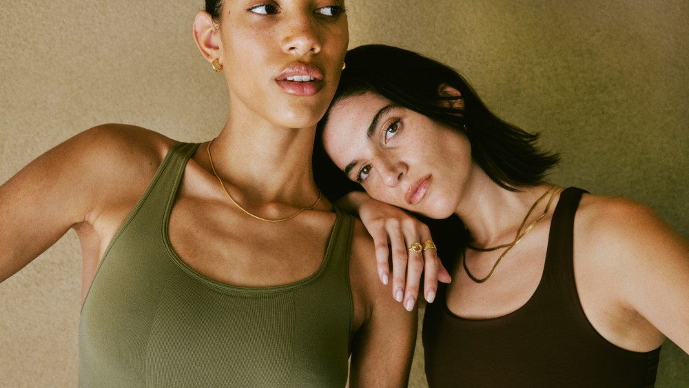A campaign image from Reformer showasing a model in a green tank and a model in a contrasting black tank. One leans on the shoulder of the other.