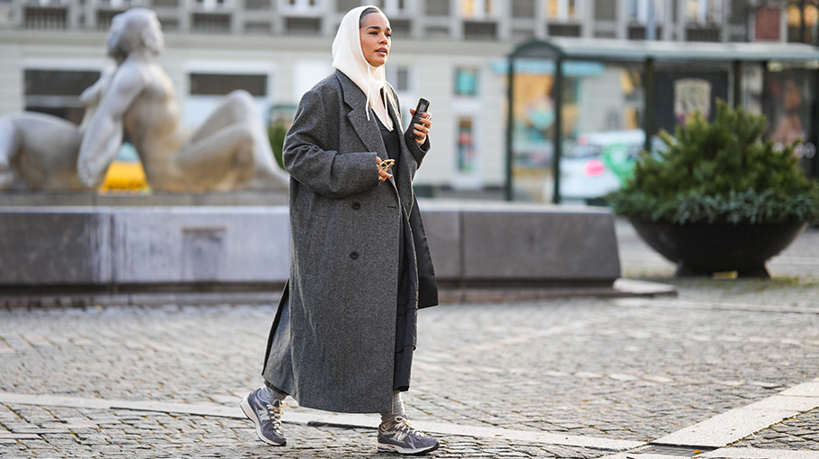A guest wears a white latte ribbed wool hoodie / balaclava, a black and white striped print pattern wool long coat, gray socks, gray sneakers from New Balance, a black nylon handbag , outside Lovechild 1979, during the Copenhagen Fashion Week Autumn/Winter 2023 on February 01, 2023 in Copenhagen, Denmark